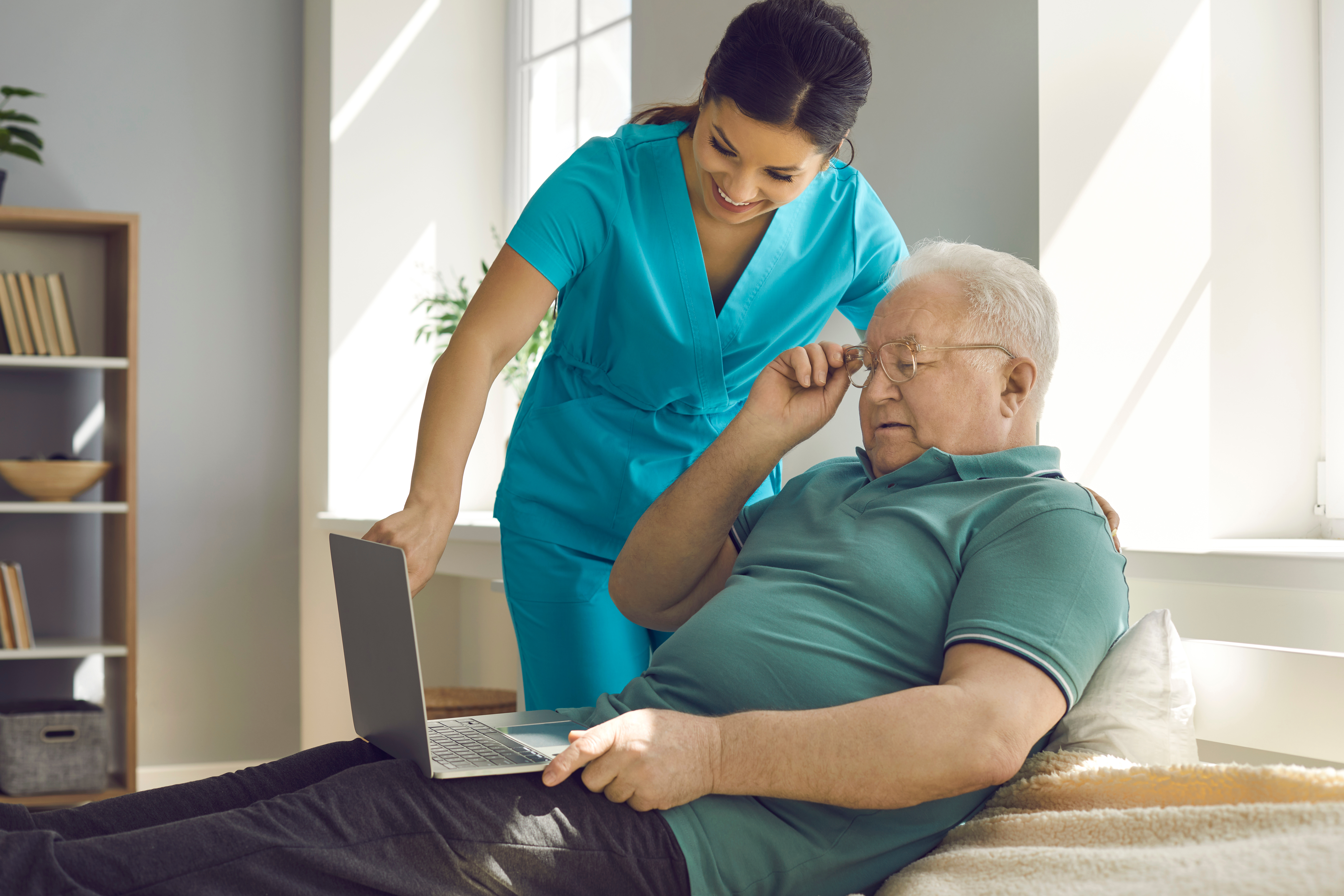 A female caregiver helping an elderly male patient use the computer.
