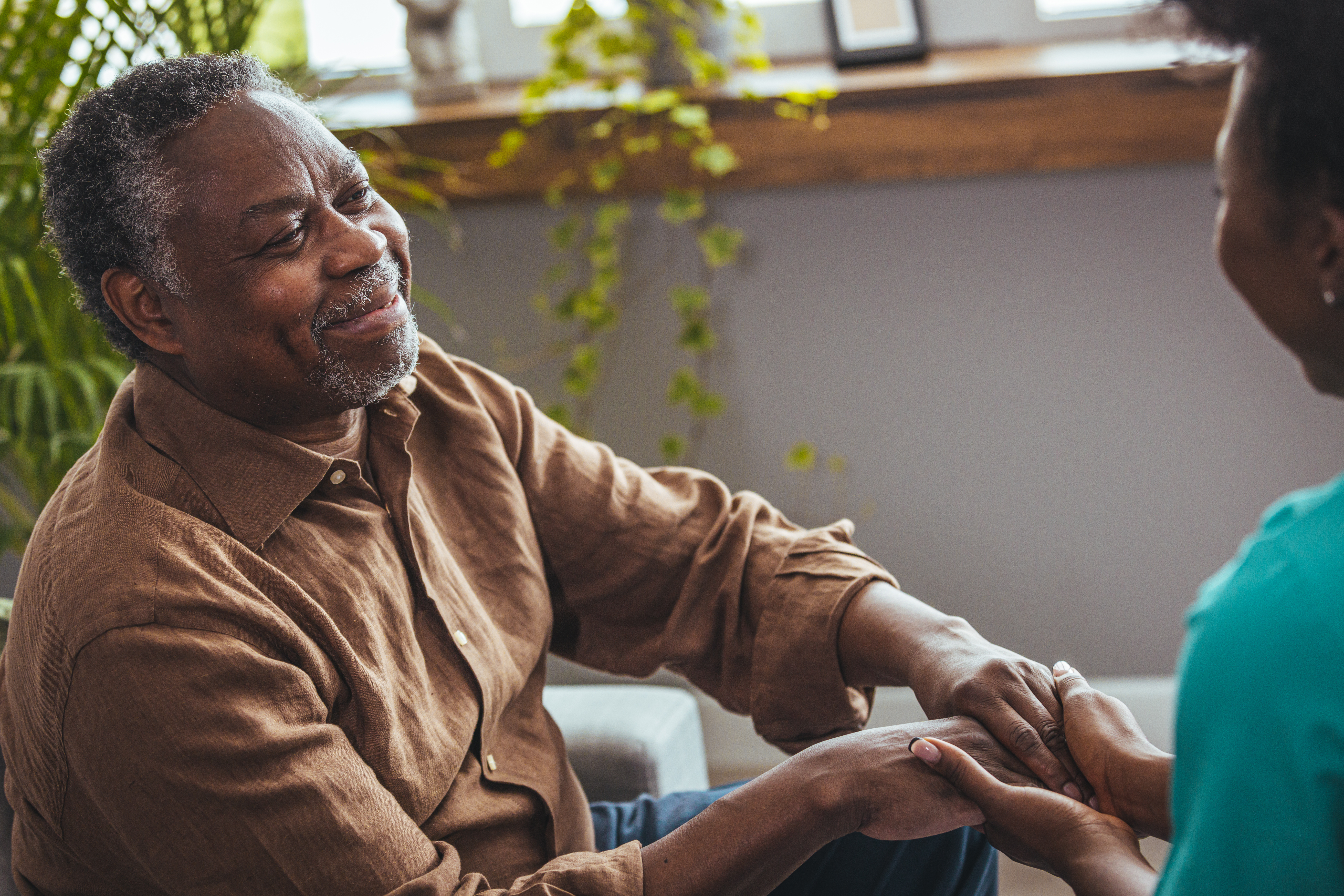 A female caregiver holds an elderly male patient's hands.