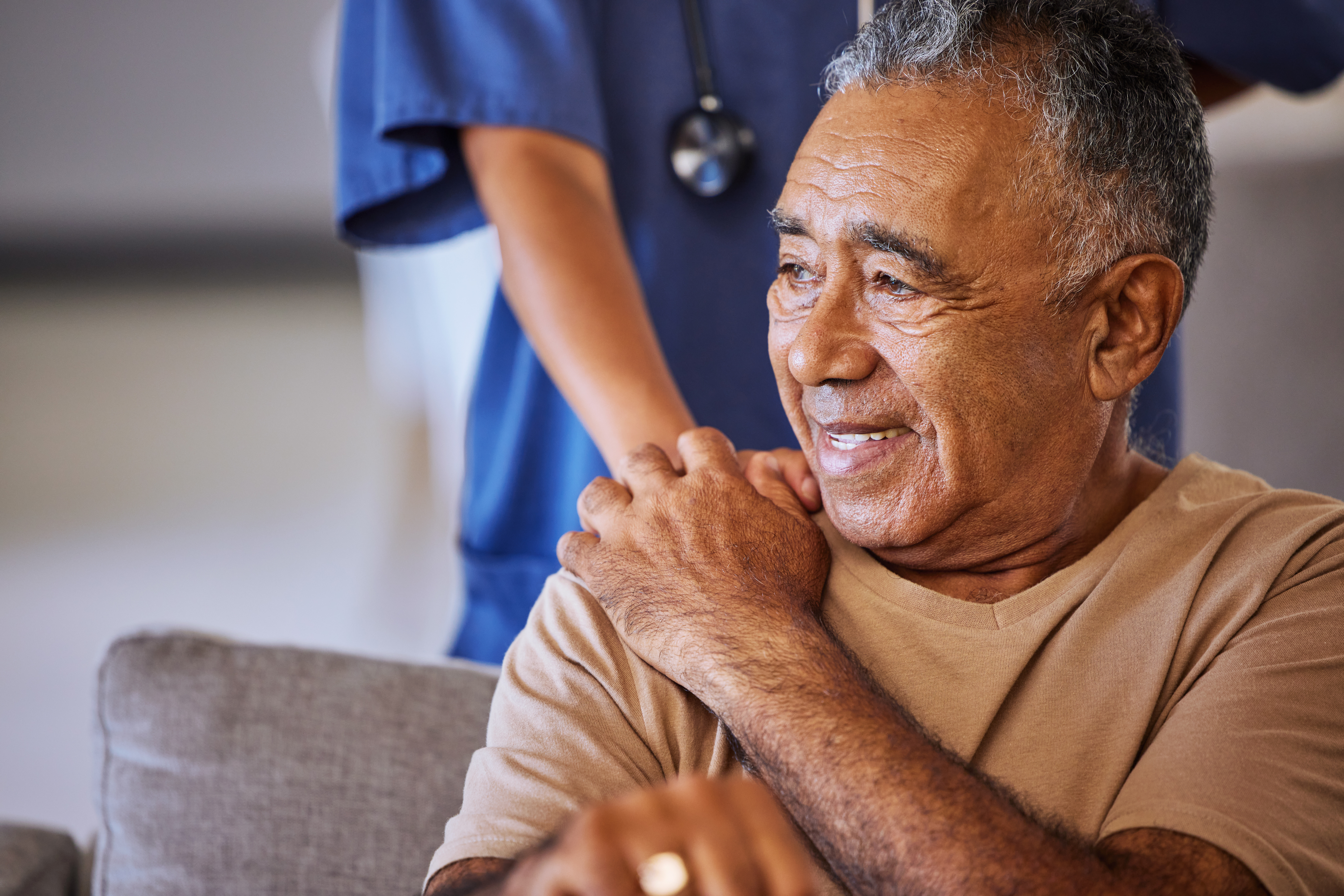 A female caregiver holds an elderly male patient's shoulder.